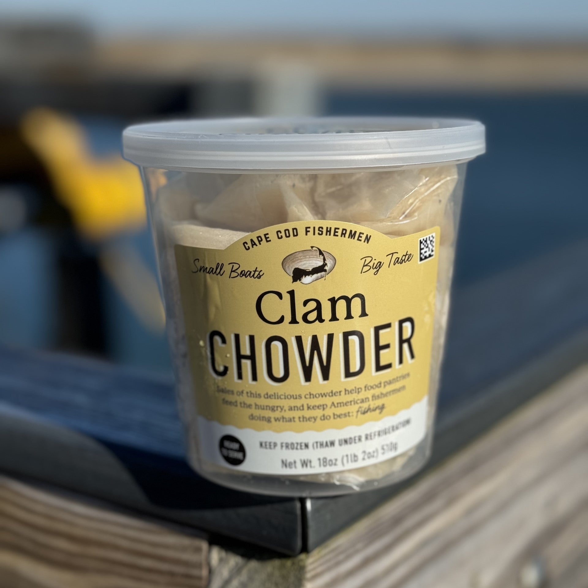 Container of Clam Chowder on a wooden surface with a blurred background