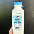 Bottle of Arruda's Heavy Cream held in a hand against a black background