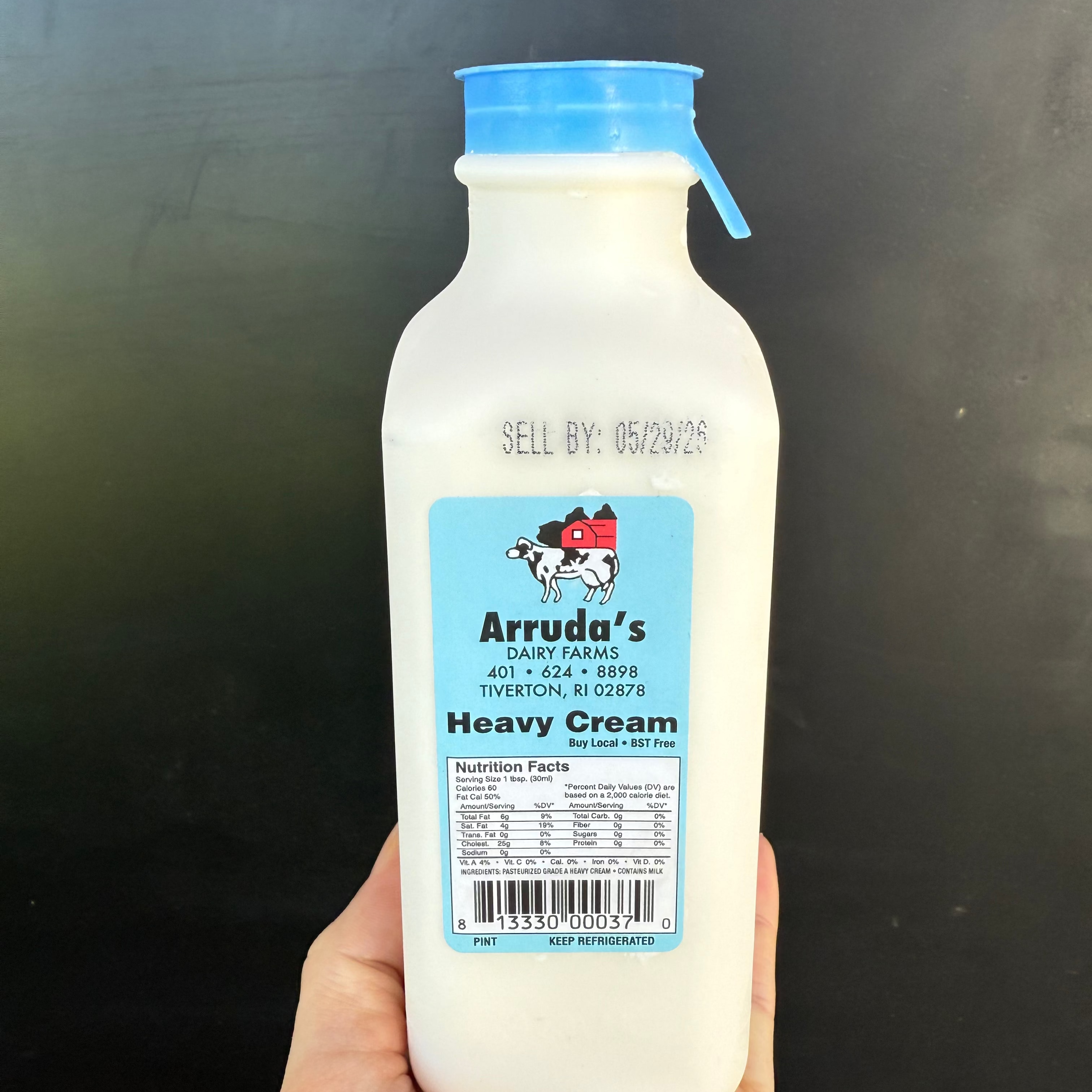 Bottle of Arruda's Heavy Cream held in a hand against a black background