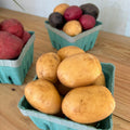 Three cartons of potatoes on a wooden surface with a white wall in the background.