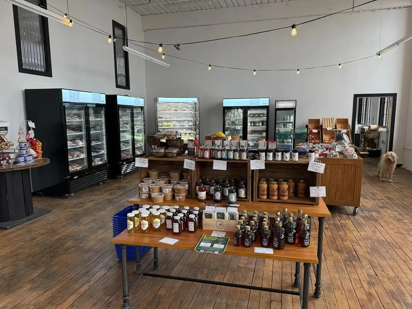 Coastal Foodshed store interior with tables displaying jars and bottles, refrigerators in background