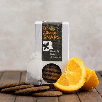 Packaged cookies labeled 'Earl Grey & Orange Snaps' with orange slices on a wooden surface.