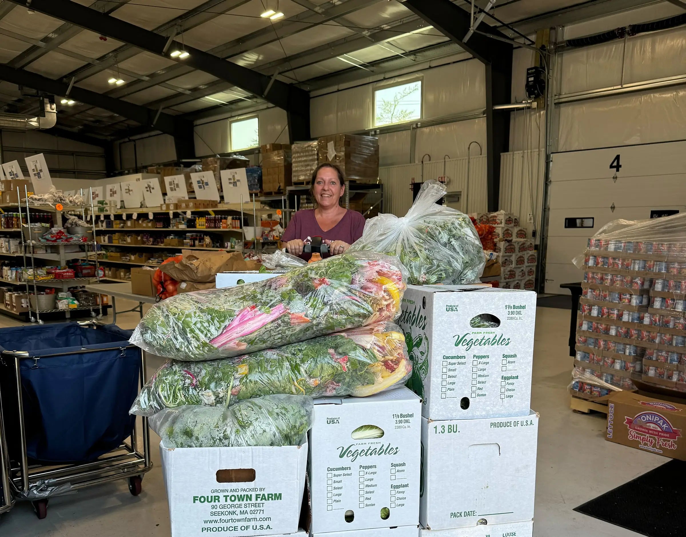 boxes & bags of assorted produce, smiling worker behind items