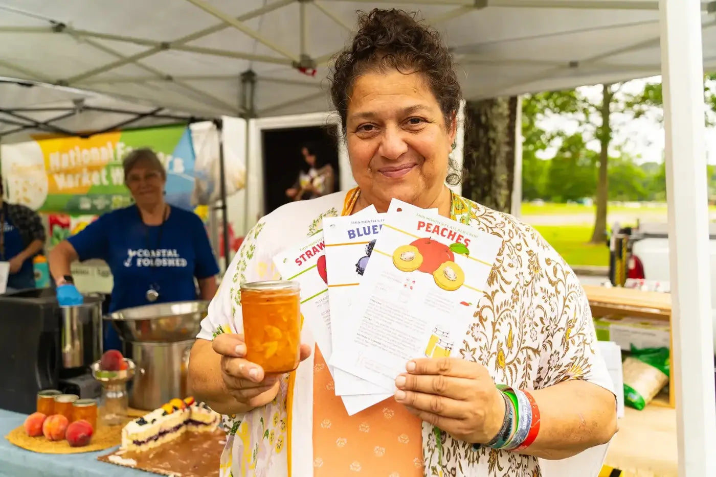 woman holding Coastal Foodshed product & colorful cards at outdoor market