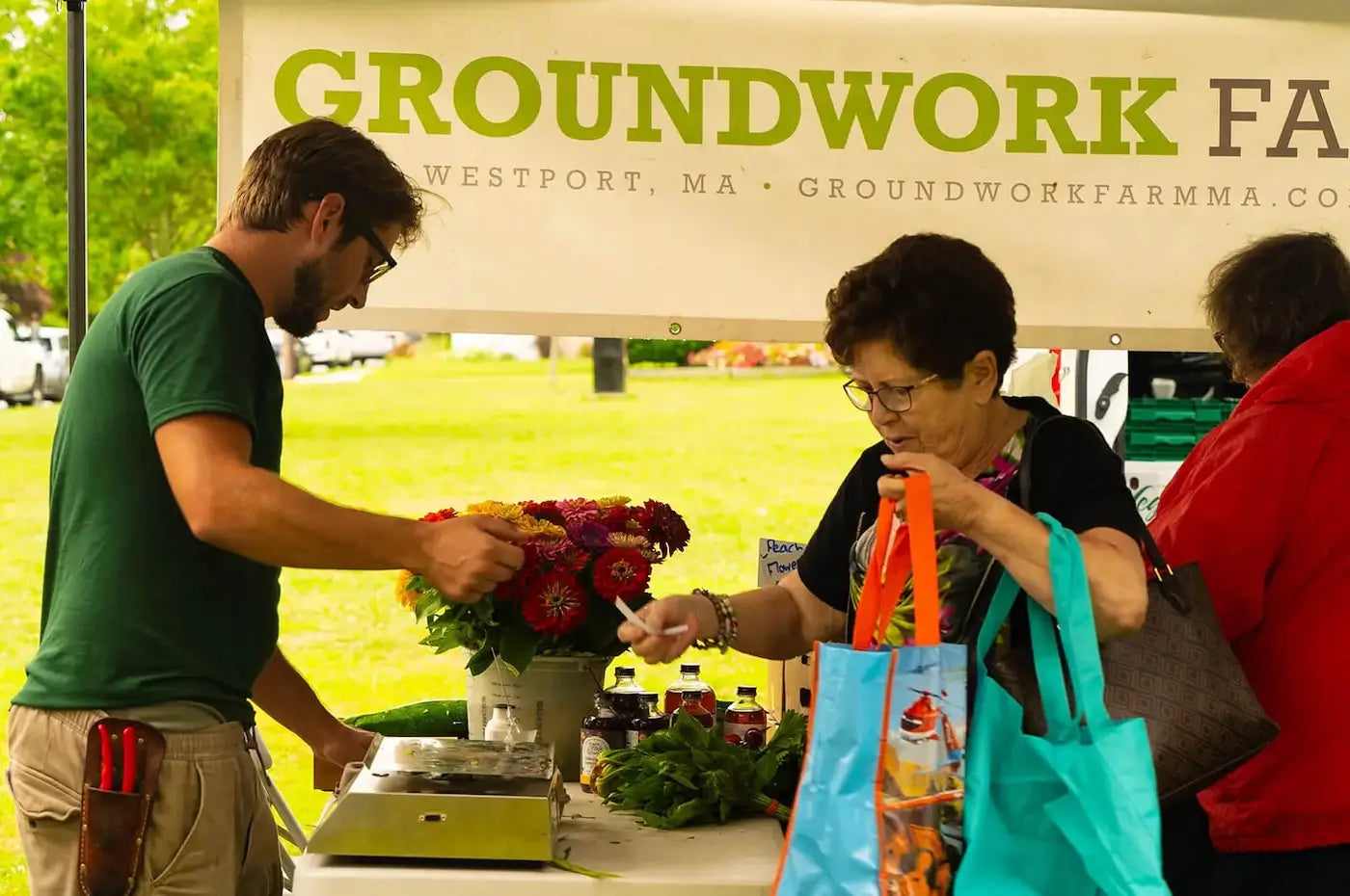 shoppers at outdoor farmer's market, Groundwork Farm banner in background